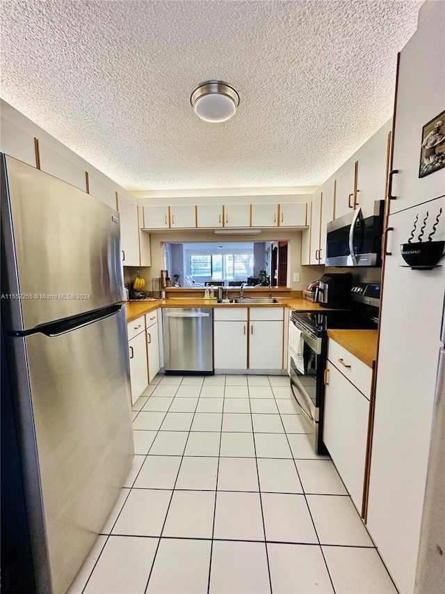 kitchen featuring a textured ceiling, white cabinetry, stainless steel appliances, and light tile patterned floors