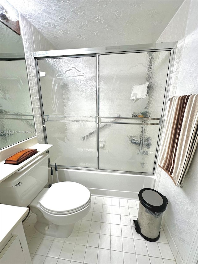 full bathroom with vanity, tile patterned floors, combined bath / shower with glass door, toilet, and a textured ceiling