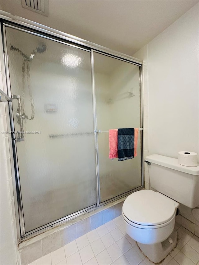 bathroom with tile patterned floors, toilet, and a shower with shower door