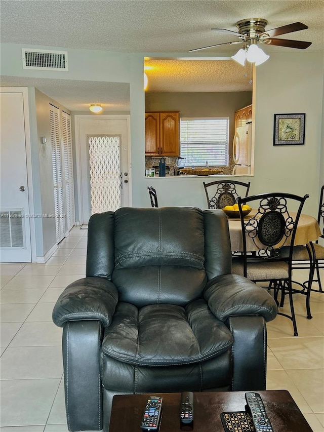 living room featuring light tile floors, ceiling fan, and a textured ceiling