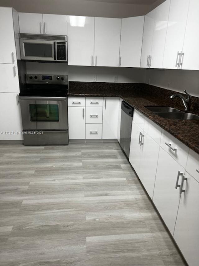 kitchen with appliances with stainless steel finishes, white cabinetry, dark stone counters, and light wood-type flooring