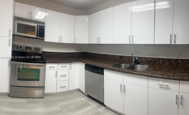 kitchen with light hardwood / wood-style flooring, stainless steel appliances, dark stone countertops, sink, and white cabinetry