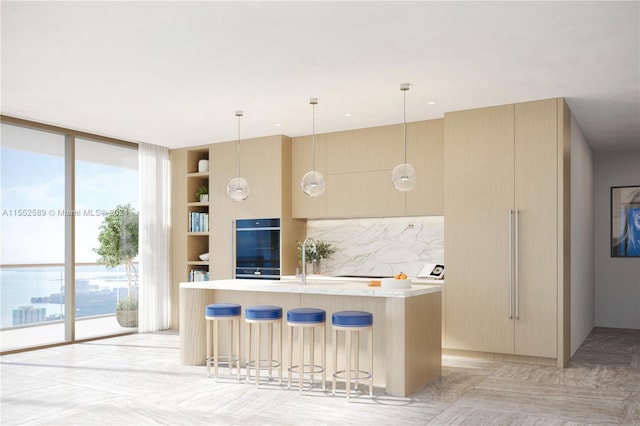 kitchen with tasteful backsplash, light brown cabinets, an island with sink, and hanging light fixtures