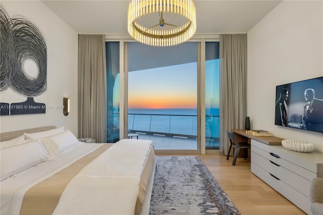 bedroom featuring expansive windows, light hardwood / wood-style flooring, access to outside, and a water view