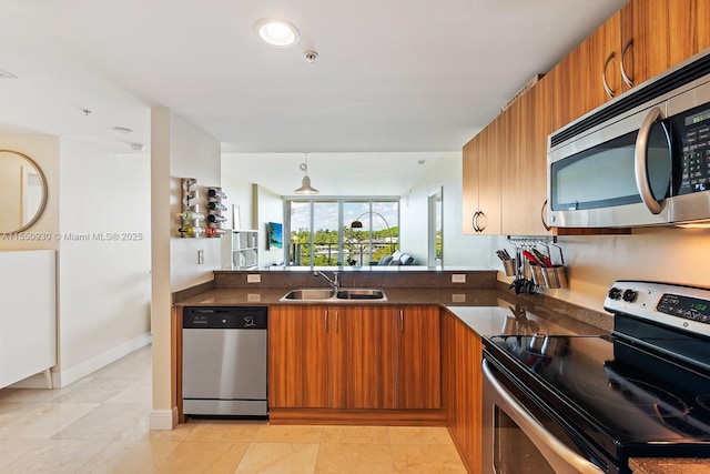 kitchen featuring brown cabinets, a sink, stainless steel appliances, dark stone counters, and a peninsula