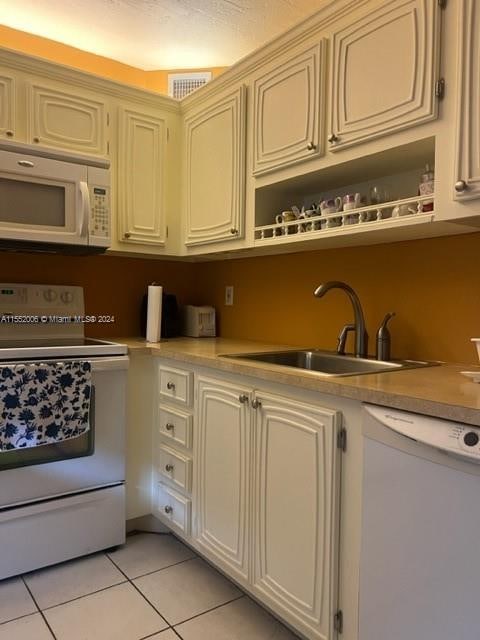 kitchen with cream cabinets, white appliances, light tile flooring, and sink