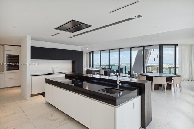 kitchen featuring light tile flooring, a water view, sink, and a kitchen island with sink