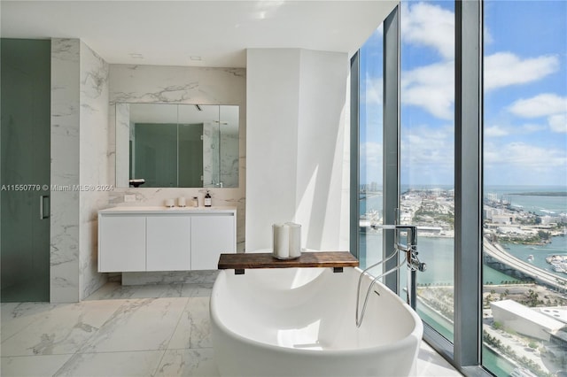 bathroom featuring tile walls, a bath to relax in, dual vanity, tile flooring, and a water view