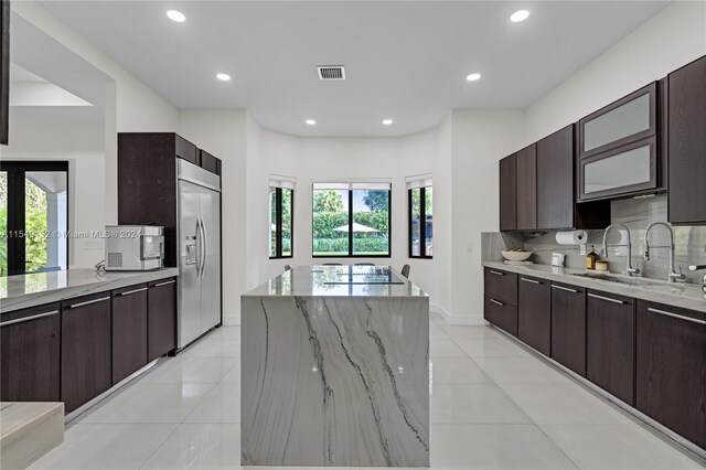 kitchen with backsplash, light stone countertops, built in fridge, and light tile floors