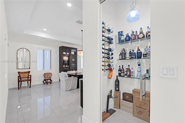 wine room featuring a raised ceiling, light tile floors, and bar area