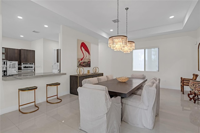 dining area with a tray ceiling, an inviting chandelier, and light tile floors