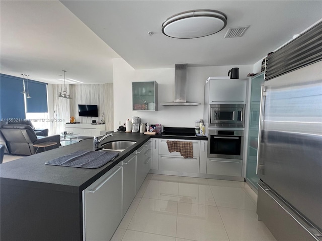 kitchen featuring a chandelier, built in appliances, wall chimney range hood, kitchen peninsula, and sink