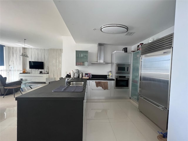 kitchen featuring built in appliances, kitchen peninsula, decorative light fixtures, and wall chimney exhaust hood