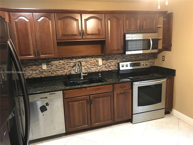 kitchen with stainless steel appliances, sink, light tile floors, and dark stone counters