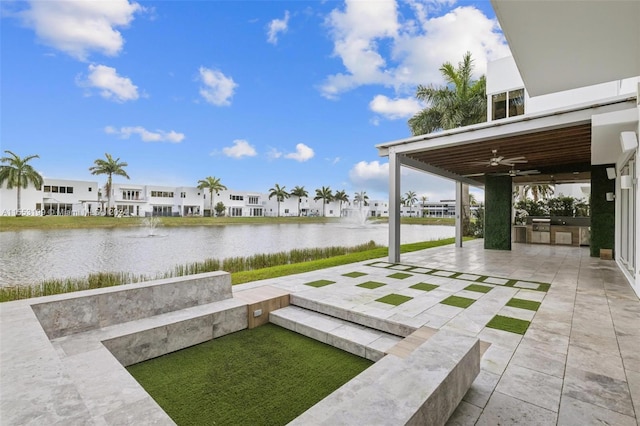 view of yard with a patio area, an outdoor kitchen, ceiling fan, and a water view