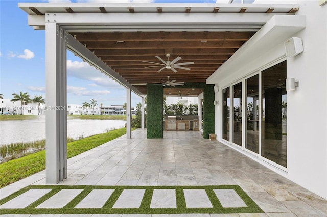 view of patio with exterior kitchen, ceiling fan, and a water view