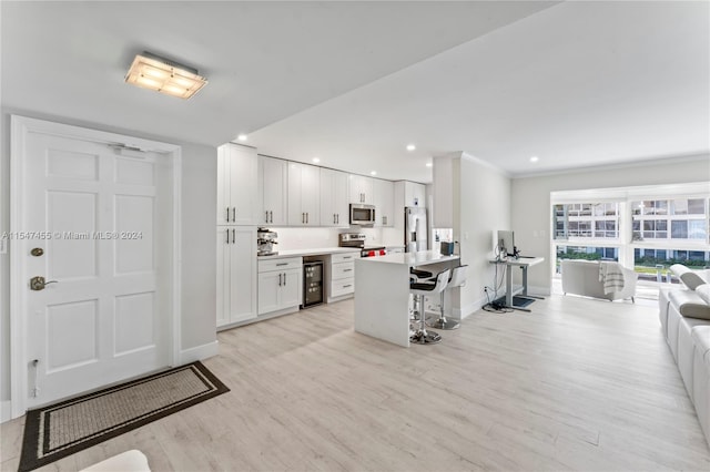 kitchen with white cabinets, stainless steel appliances, light hardwood / wood-style floors, and a kitchen bar