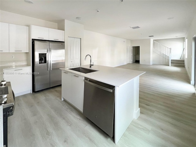 kitchen featuring appliances with stainless steel finishes, white cabinets, a kitchen island with sink, light wood-type flooring, and sink