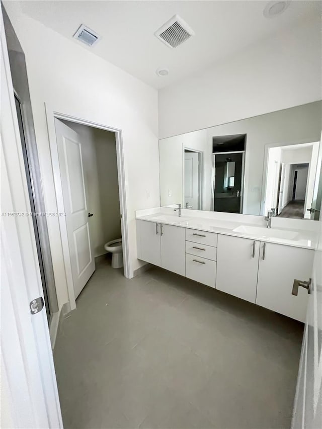 bathroom with toilet, double vanity, concrete flooring, and a bidet