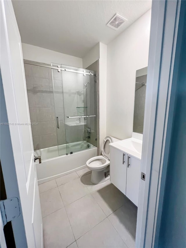 full bathroom featuring toilet, a textured ceiling, vanity, enclosed tub / shower combo, and tile floors