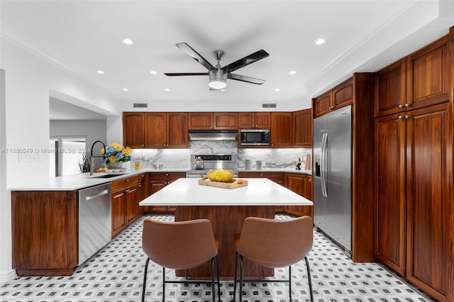 kitchen featuring ceiling fan, a kitchen bar, stainless steel appliances, and crown molding