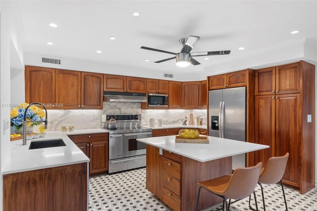 kitchen with crown molding, appliances with stainless steel finishes, sink, ceiling fan, and a kitchen island