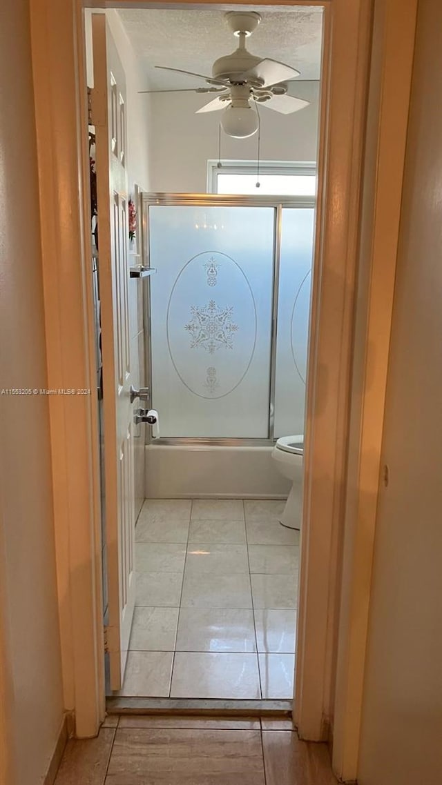 bathroom featuring ceiling fan, a textured ceiling, bath / shower combo with glass door, tile patterned floors, and toilet