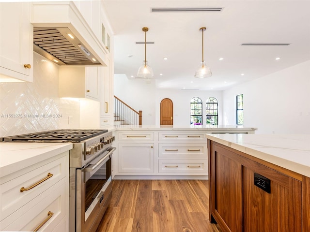 kitchen with white cabinetry, stainless steel range, light hardwood / wood-style floors, decorative light fixtures, and custom range hood