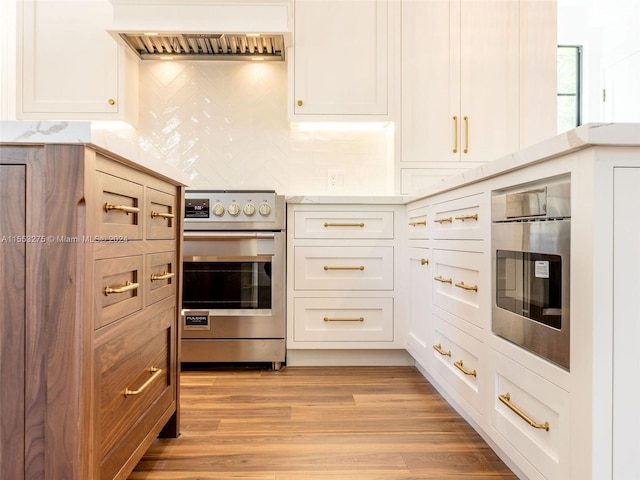 kitchen with light wood-type flooring, white cabinetry, stainless steel appliances, and premium range hood