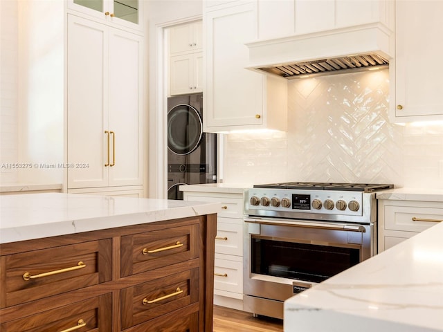 kitchen featuring custom exhaust hood, white cabinets, stainless steel stove, tasteful backsplash, and stacked washer / dryer