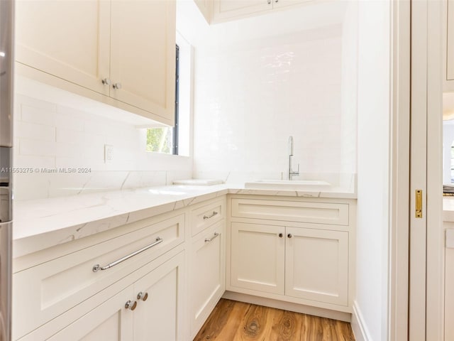 kitchen featuring backsplash, sink, light hardwood / wood-style flooring, cream cabinetry, and light stone counters