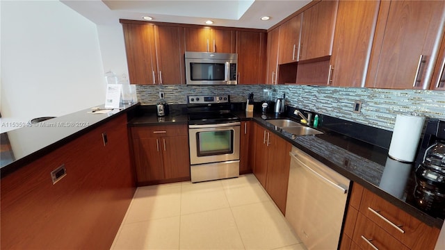 kitchen featuring backsplash, light tile flooring, sink, stainless steel appliances, and dark stone countertops