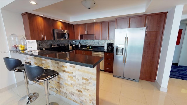 kitchen featuring kitchen peninsula, light tile flooring, appliances with stainless steel finishes, tasteful backsplash, and a breakfast bar area