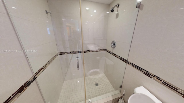 bathroom with tile walls, toilet, and a shower with shower door