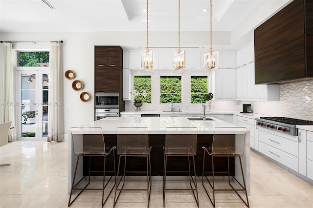 kitchen with a kitchen bar, dark brown cabinets, stainless steel appliances, sink, and a center island with sink