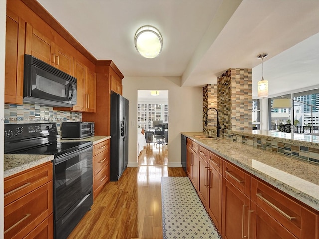 kitchen with sink, light hardwood / wood-style floors, black appliances, tasteful backsplash, and decorative light fixtures