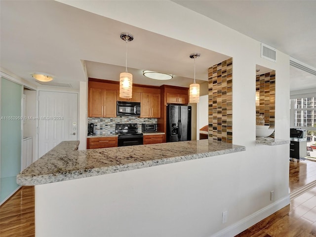 kitchen featuring kitchen peninsula, black appliances, backsplash, hanging light fixtures, and light wood-type flooring