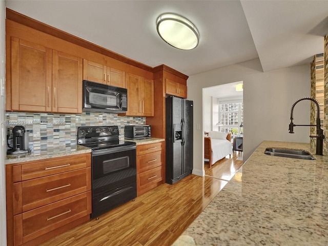 kitchen with light hardwood / wood-style floors, sink, light stone counters, and black appliances