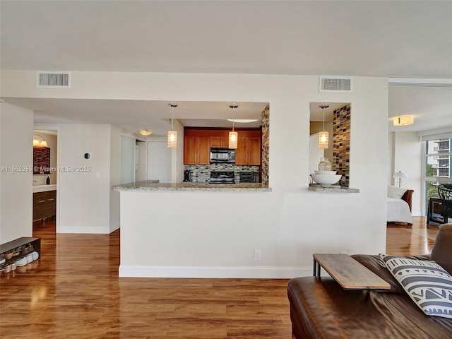 kitchen with pendant lighting, range, backsplash, light stone counters, and kitchen peninsula