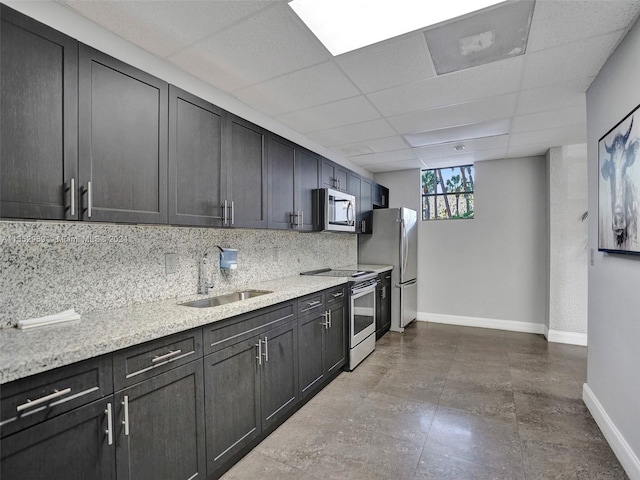 kitchen featuring sink, light stone counters, appliances with stainless steel finishes, a drop ceiling, and tasteful backsplash