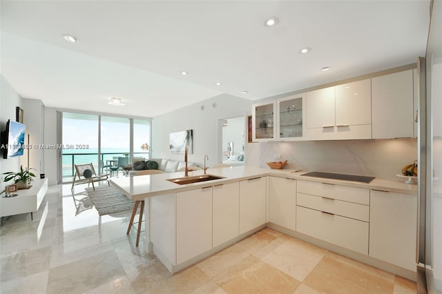 kitchen featuring a wall of windows, sink, black electric cooktop, light tile flooring, and a water view