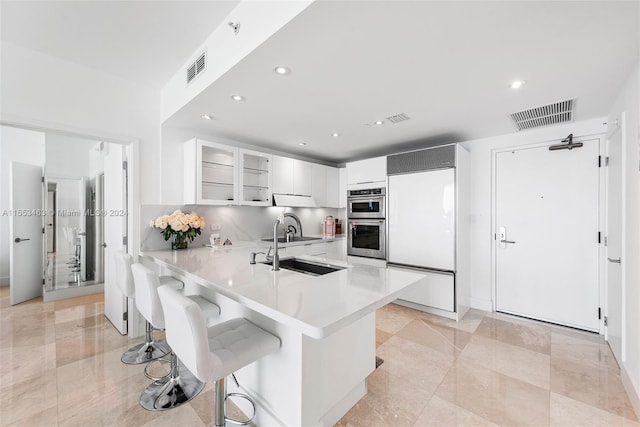 kitchen with paneled refrigerator, light tile floors, white cabinets, a breakfast bar area, and double oven