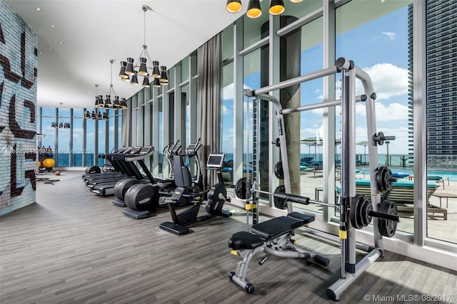 exercise room featuring an inviting chandelier, a wealth of natural light, a wall of windows, and hardwood / wood-style flooring