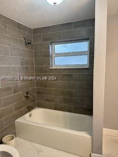 bathroom with tiled shower / bath, toilet, tile walls, and a textured ceiling