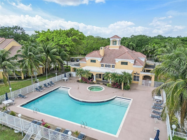 community pool with a patio, a hot tub, and fence