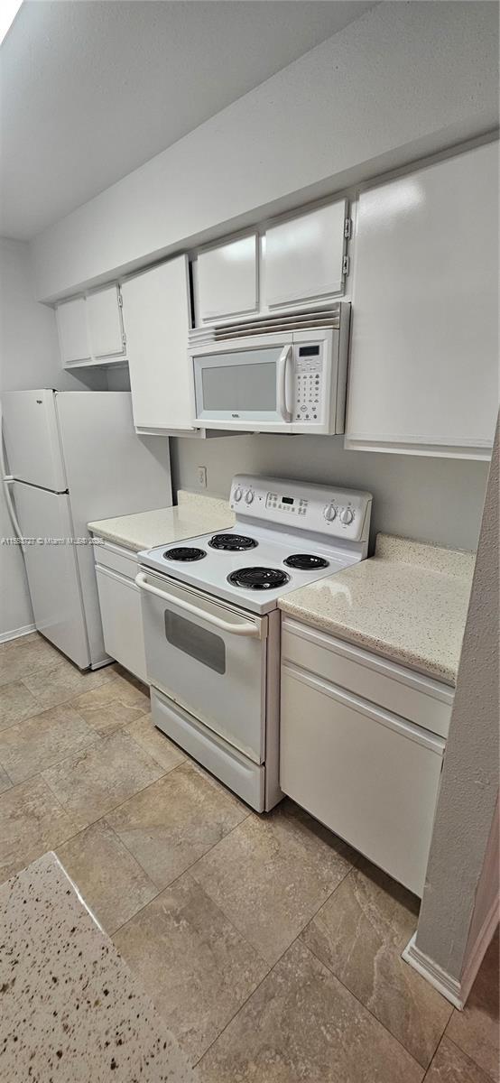 kitchen with white appliances, white cabinetry, and baseboards