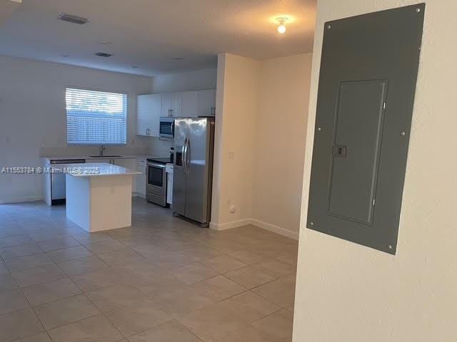 kitchen featuring sink, appliances with stainless steel finishes, white cabinetry, electric panel, and a center island