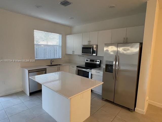 kitchen with white cabinetry, stainless steel appliances, a center island, and sink