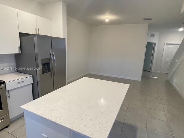 kitchen with light tile patterned floors, stainless steel fridge with ice dispenser, a kitchen island, and white cabinets