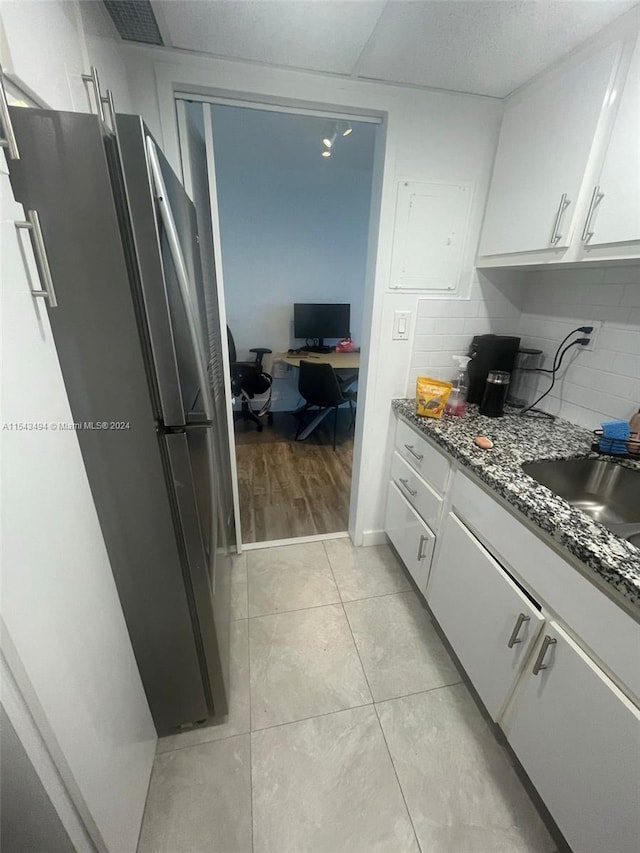 kitchen featuring white cabinetry, backsplash, stainless steel fridge, light hardwood / wood-style floors, and dark stone counters